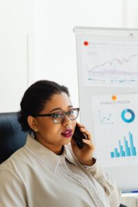 African American woman in office, analyzing finance charts on white board, talking on phone.